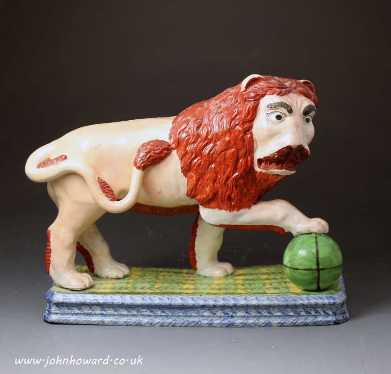 A rare and previously unrecorded pearlware Staffordshire pottery figure of a lion standing on a base with a paw on sphere. The naive bold modeling and decoration of this figure is especially unusual and striking.