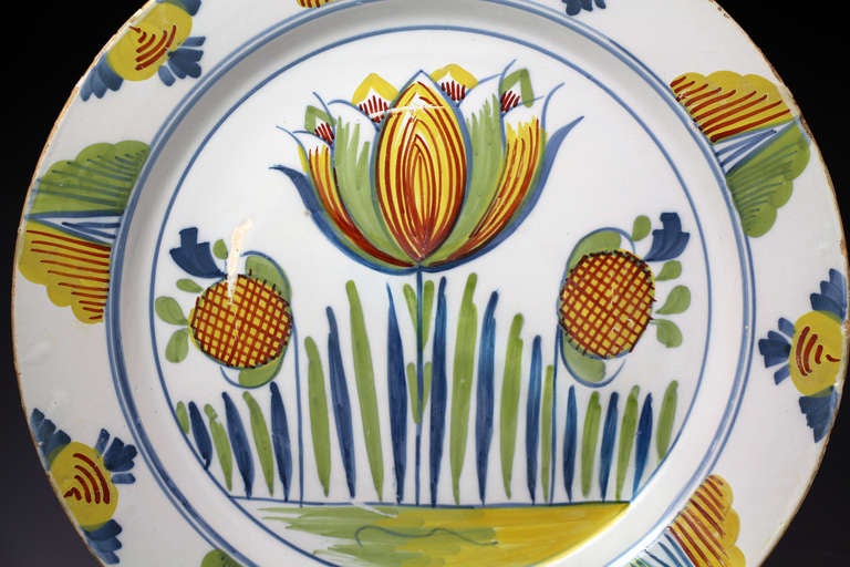 Antique period delftware pottery charger well decorated with a tulip in polychrome colours. 

Bristol.