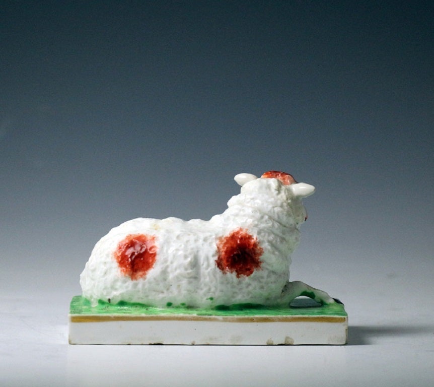 A porcelain figure of a ewe recumbent on an oblong base decorated on top with green and a gilt line along border.