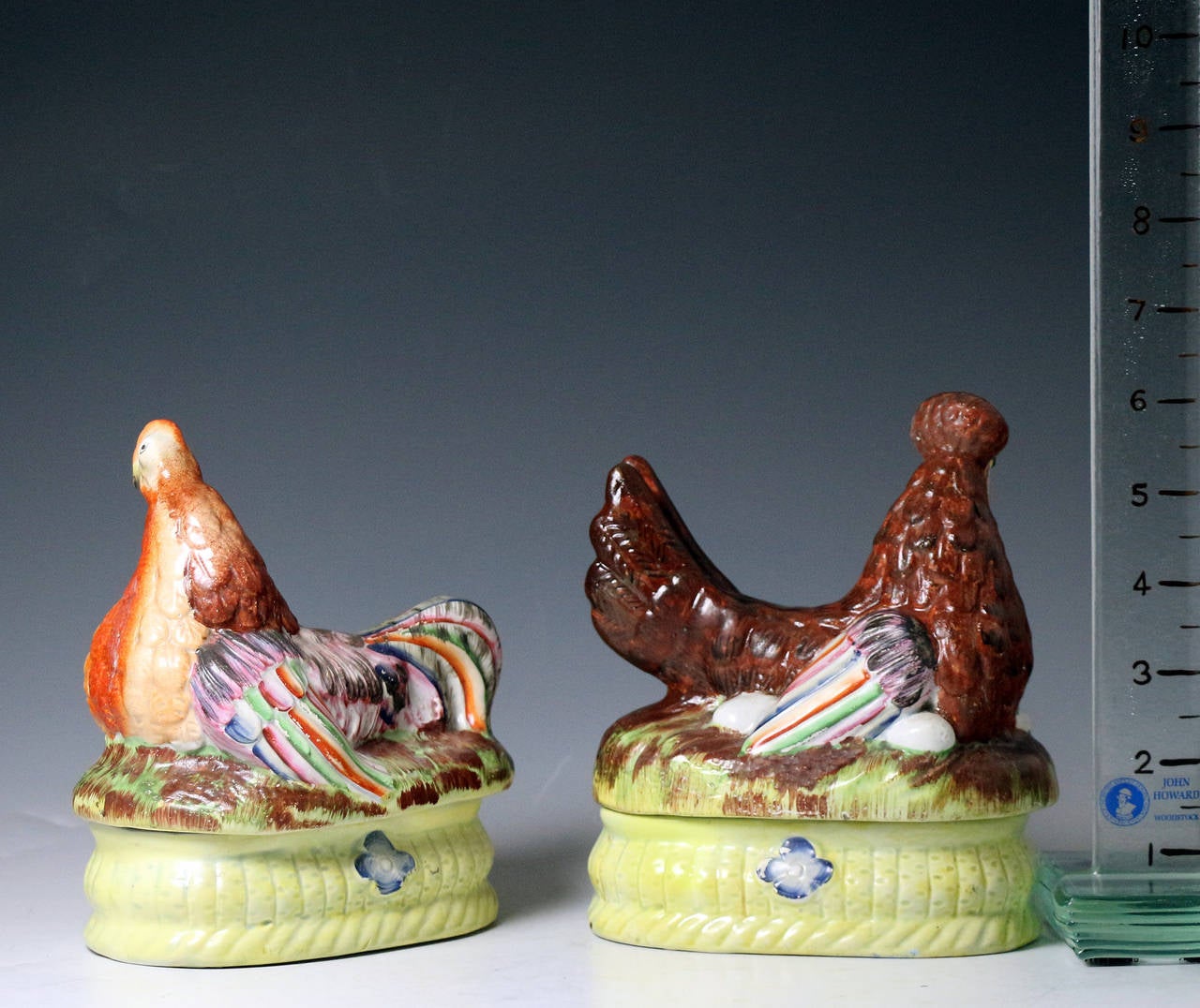 A rare pair of antique Staffordshire pottery figures of hens each sitting on yellow baskets with a blue flower. 
This pair brightly coloured and rather comical pair are the rarest form of hen on nests produced by the Staffordshire potters.