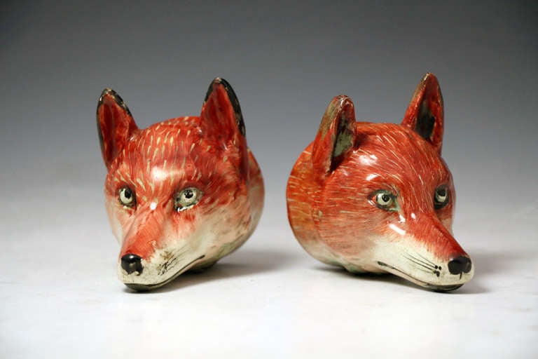 A pair of antique Staffordshire pottery pearlware stirrup cups in the form of foxes heads. 
A pair of cups are rare and these examples capture the spirit and character of the fox perfectly. 