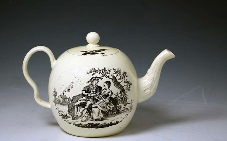 Antique English creamware pottery teapot with an underglaze black printed scene of a couple seated in a garden the woman playing a flute. The cover is decorated with an image of a bird and winged insect.Attributed to Greatbach Pottery Staffordshire.