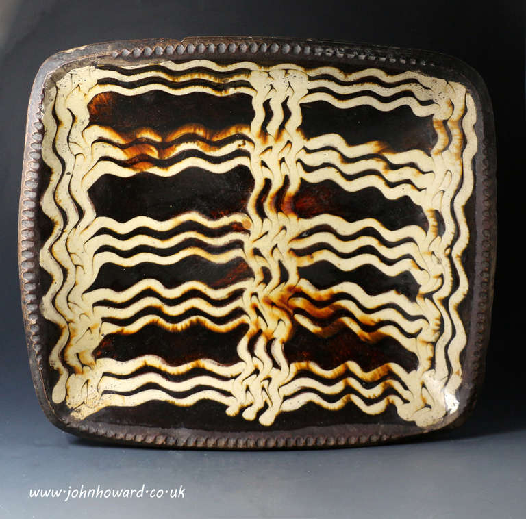 Antique English pottery slipware baking or loaf dish mid 18th century.
This fine and very rare earthenware dish is exceptionally well decorated with a creamy slip which is enhanced by the dark chocolate ground. 

Provenance: From the private