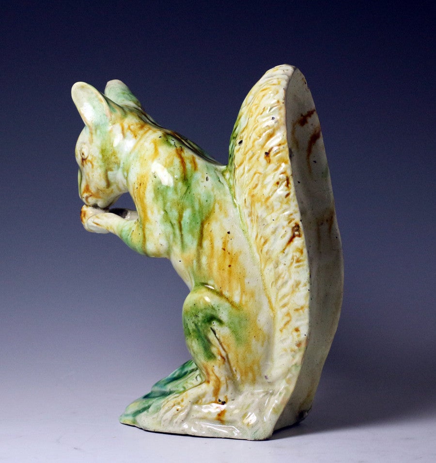 A rare and very charming Staffordshire pottery figure of a seated squirrel nibbling a nut. 
The figure is strongly decorated in green and mustard oxide glazes on an earthenware creamware body.