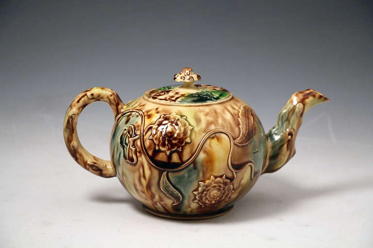 Antique Staffordshire cream-coloured pottery teapot and cover, England c1765. 
The teapot is a classic globular shape with typical Thomas Whieldon type tortoise-shell glazes over a relief molded flower and vine decoration body. 

Provenance: