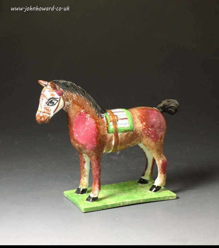 A fine and rare example of an antique English pottery figure of a well decorated horse which is modeled standing on a thin green base. The figure was produced at the turn of the 18th and 19th century. This model if perhaps the most charming and