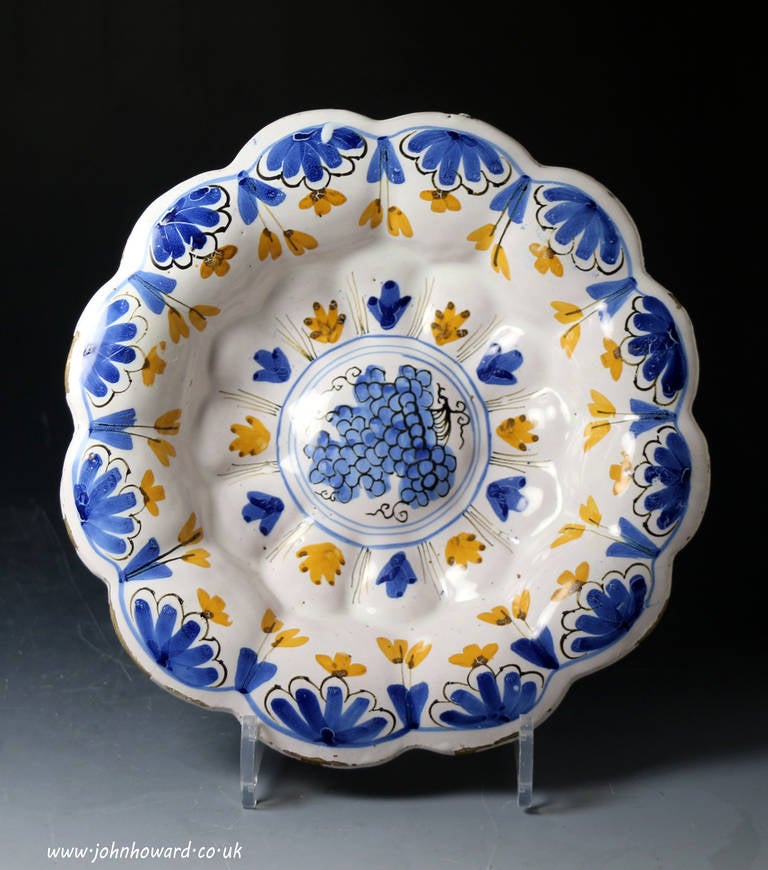 A molded lobed delftware pottery dish decorated with a bunch of grapes in a central panel. Late 17th century period.