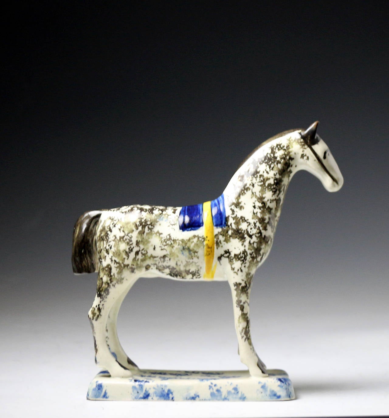 Pearlware glaze pottery figure of horse standing on an oblong base. 
The base and figure which has a blue saddle are sponge decorated. 
The figure has an elegant stance with a handsome charm. 
This rare piece still retains the famous