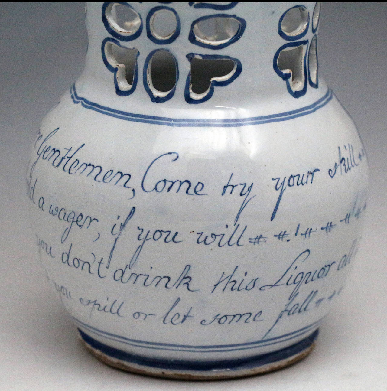 A good English delftware pottery puzzle jug decorated in cobalt blue with chinoserie images. 
The jug is globular form with a cylindrical neck which is pierced with naive like flower heads with heart shaped petals. 
The jug is also decorated with
