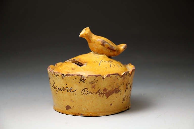 A rare and charming pottery money bank with a bird perched on top. 
The money box is inscribed 