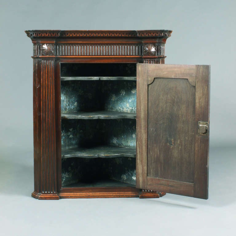 A George III Chippendale period mahogany hanging corner cupboard of a good original colour and patina; architectural detail in the cornice with greek key detail, fluted frieze, pilasters and carved flower paterae; arched fielded panel doors.