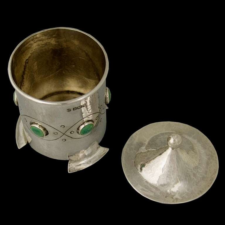 A very good example of an Edwardian Arts & Crafts silver tea caddy with a detachable cone-shaped lid with silver ball finial. The surface having a spot hammered finish and the body decorated with chased chain decoration inter-spaced with green