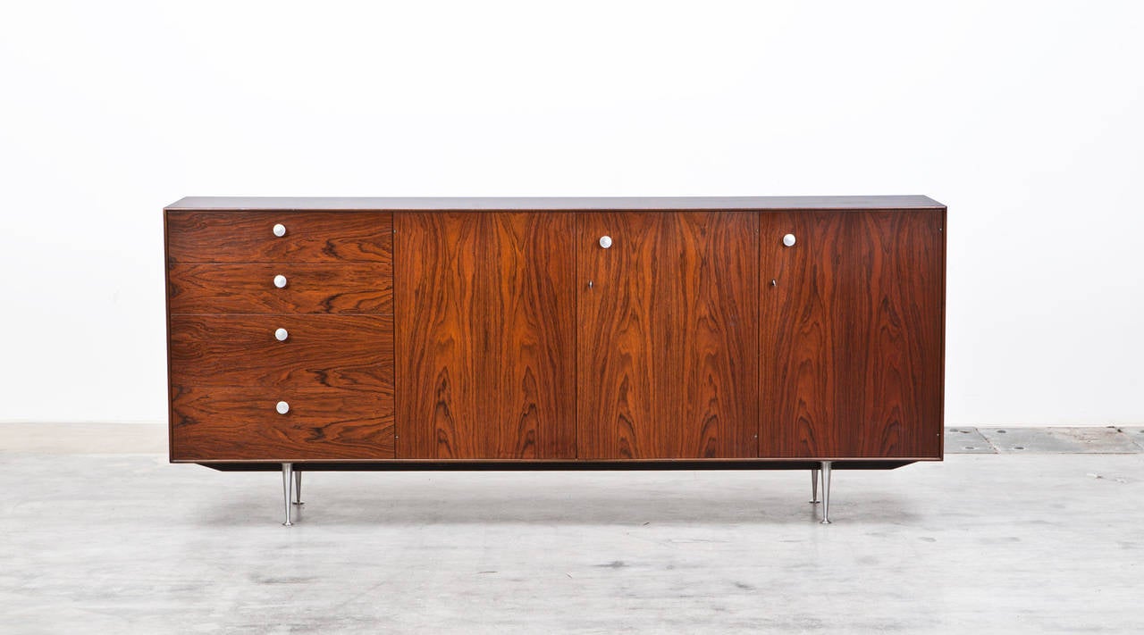 Thin edge wooden credenza with four drawers and two doors opening to reveal adjustable shelves and open storage space. Aluminium tapering legs. Manufactured by Herman Miller.