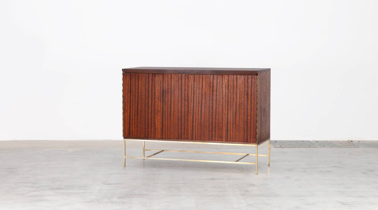 A timeless Sideboard designed by american Paul McCobb with fold doors concealing six smaller drawer trays and one big. Corpus and doors are in walnut and stands on  brass square tube base. Manufactured by Calvin.