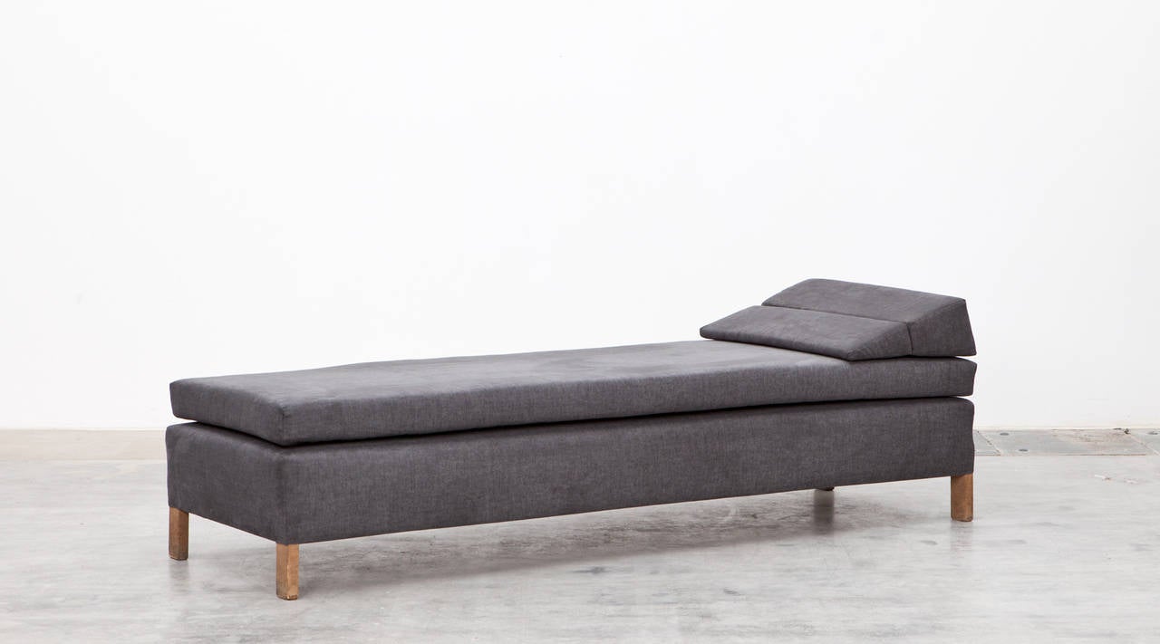 This daybed was designed by German modernist Ferdinand Kramer in 1953 for Johann-Wolfgang-Goethe University in Frankfurt am Main, and has a wedge-shaped headrest that folds up into an armrest. The daybed is newly upholstered with high-quality