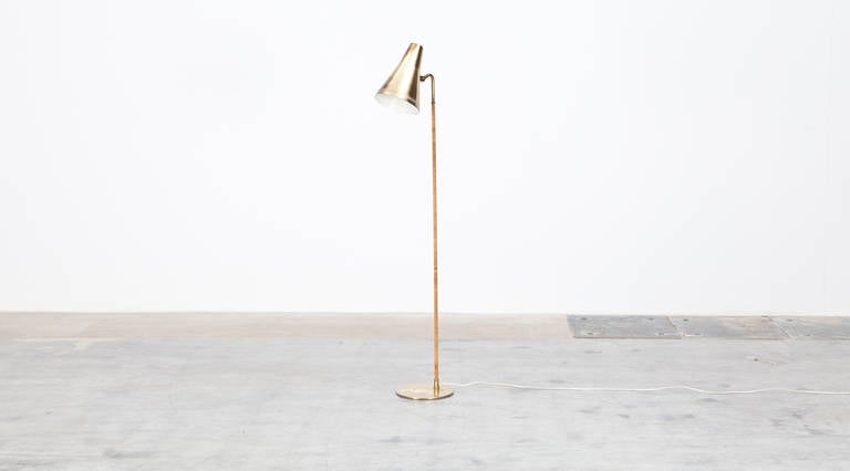 This Paavo Tynell floor lamp in its outstanding design comes with a adjustable shade made out of brass same like the round base. The stem is wrapped with leather. Manufactured by Taito Oy.
