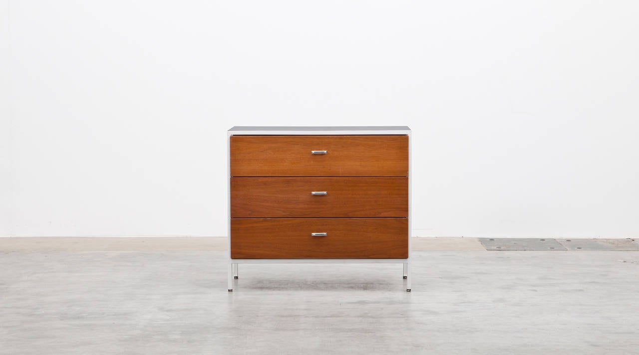 The Pair of George Nelson Commode comes in a white metal frame. The three drawers are walnut and decorated with oval chrome handles. The sides and the back are laminated. Manufactured by Herman Miller.