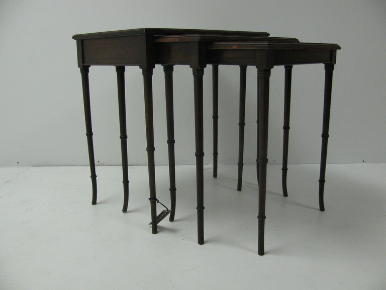 Set of three faux bamboo mahogany tables. Legs taper and flare at bottom. Larger table has a black glass top.