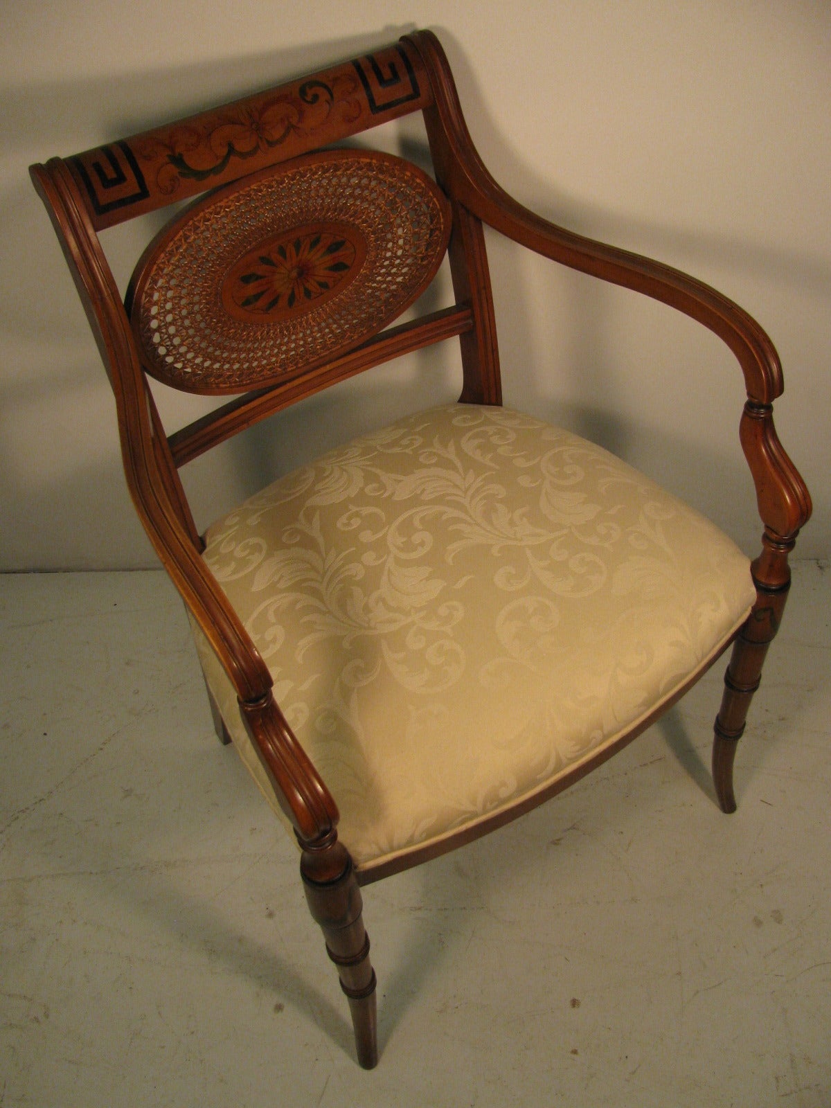 Beautiful and elegant pair of caned oval back armchairs. Hand-painted crest and legs. Carved reeded legs with curved arms. Very well proportioned. Reupholstered seats in a period style damask. A quality pair in every manner. In excellent vintage