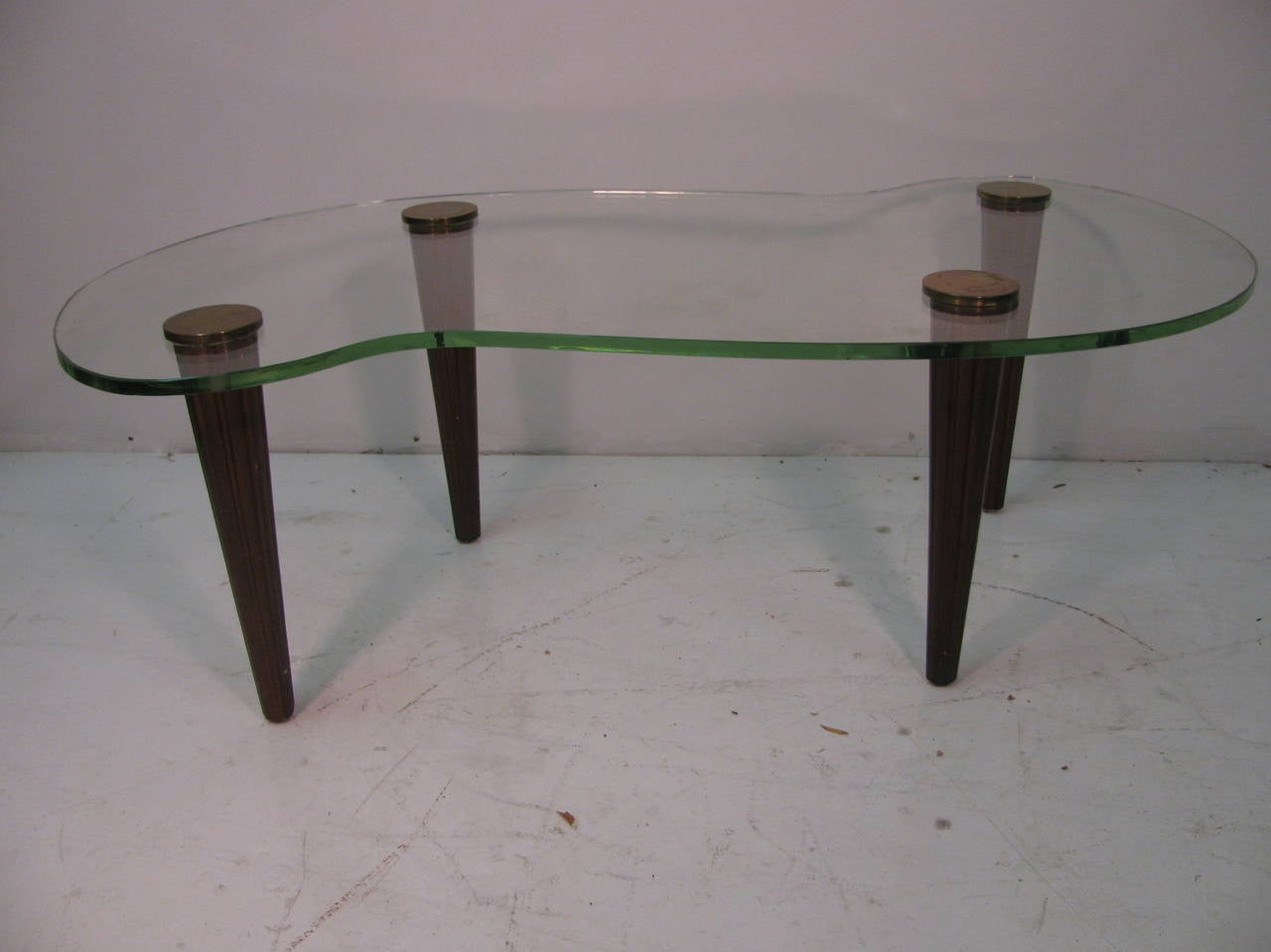 Beautiful glass top cocktail table in the style of Gilbert Rohde. Tapered, fluted legs with brass caps locking them to the glass top.