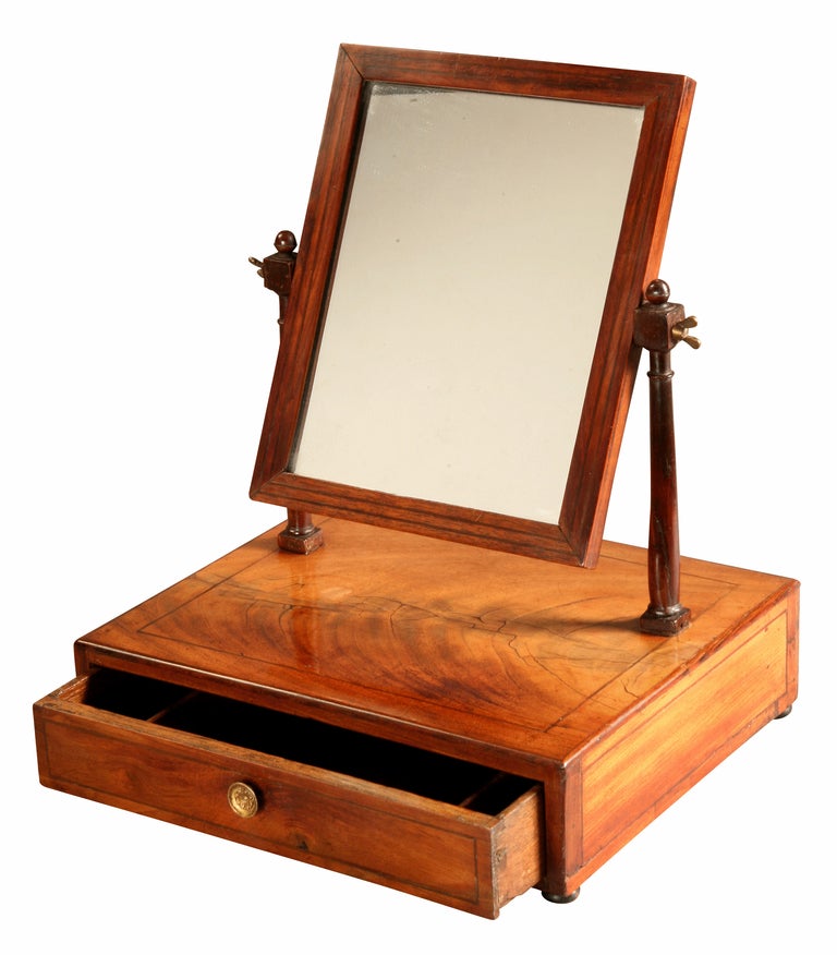 A mahogany Toilet Mirror with stringing decoration which has faded in colour. To dismantle the mirror the wing bolts that support the glass on the columns are removed. These bolts also allow the mirror to be angled. With the mirror removed the acorn