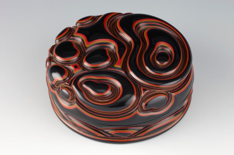 Kogo or container for incense in a compressed, circular form ornamented in deep relief with an abstract motif of rocks and swirling waves. Of layered and carved red, tan and black lacquers over a linen base, the interior in black lacquer. Signed on