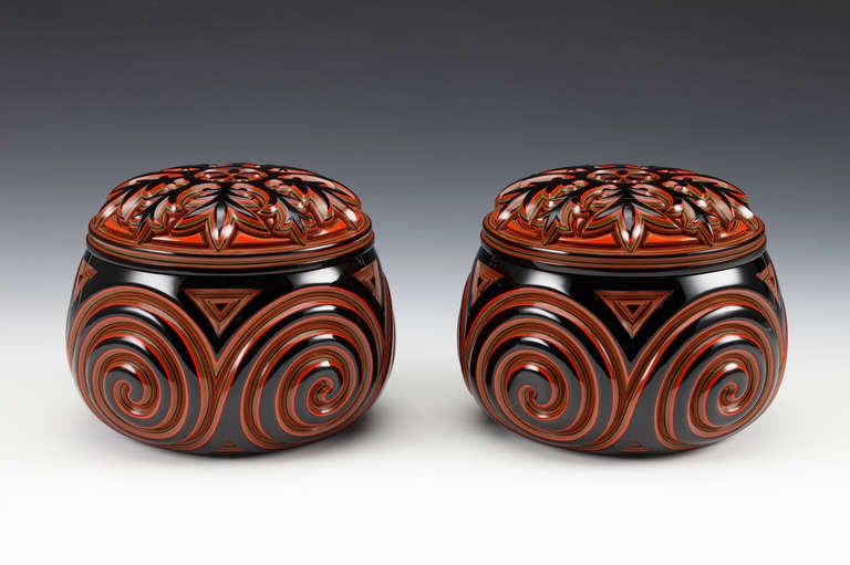 Pair of boxes for the black and white playing stones for the game of go (go-ishi-ire or go stone containers), ornamented on the sides with deep-relief, abstract whirlpool designs and on the top with a stylized floral motif surrounding a central mon
