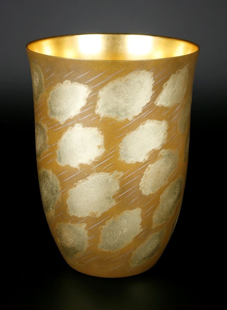 Vase in a tall and flaring cylindrical form, ornamented on the sides with stylized clouds and slanting rain. Of cast bronze, the rain inlaid with silver in shallow nunome technique, the background warmed with a rubbed, matte gilt finish, and the