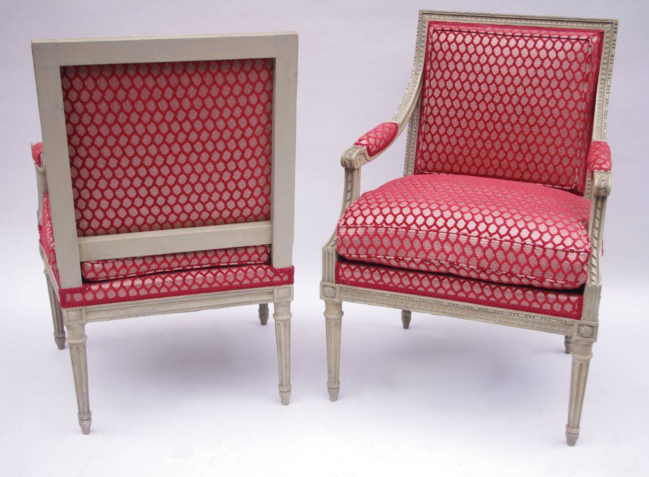 Pair of à la Reine Louis XVI style armchairs in carved and grey lacquered wood standing on four fluted tapered legs. Uprights adorned with fusarolles and water leaves friezes, twisted ribbons and triglyphs on the armrest support and rosette