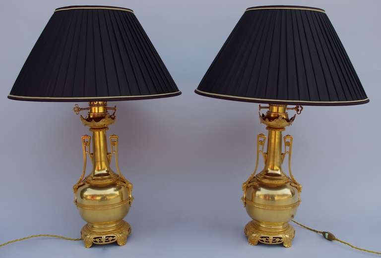 Pair of gilt brass and bronze bottle-shaped lamps with Etruscan style handles, standing on a Chinese style circular openwork base. The belly is decorated with a discreet fluted frieze framed by pearls, from which start high palmettes handles.

Work
