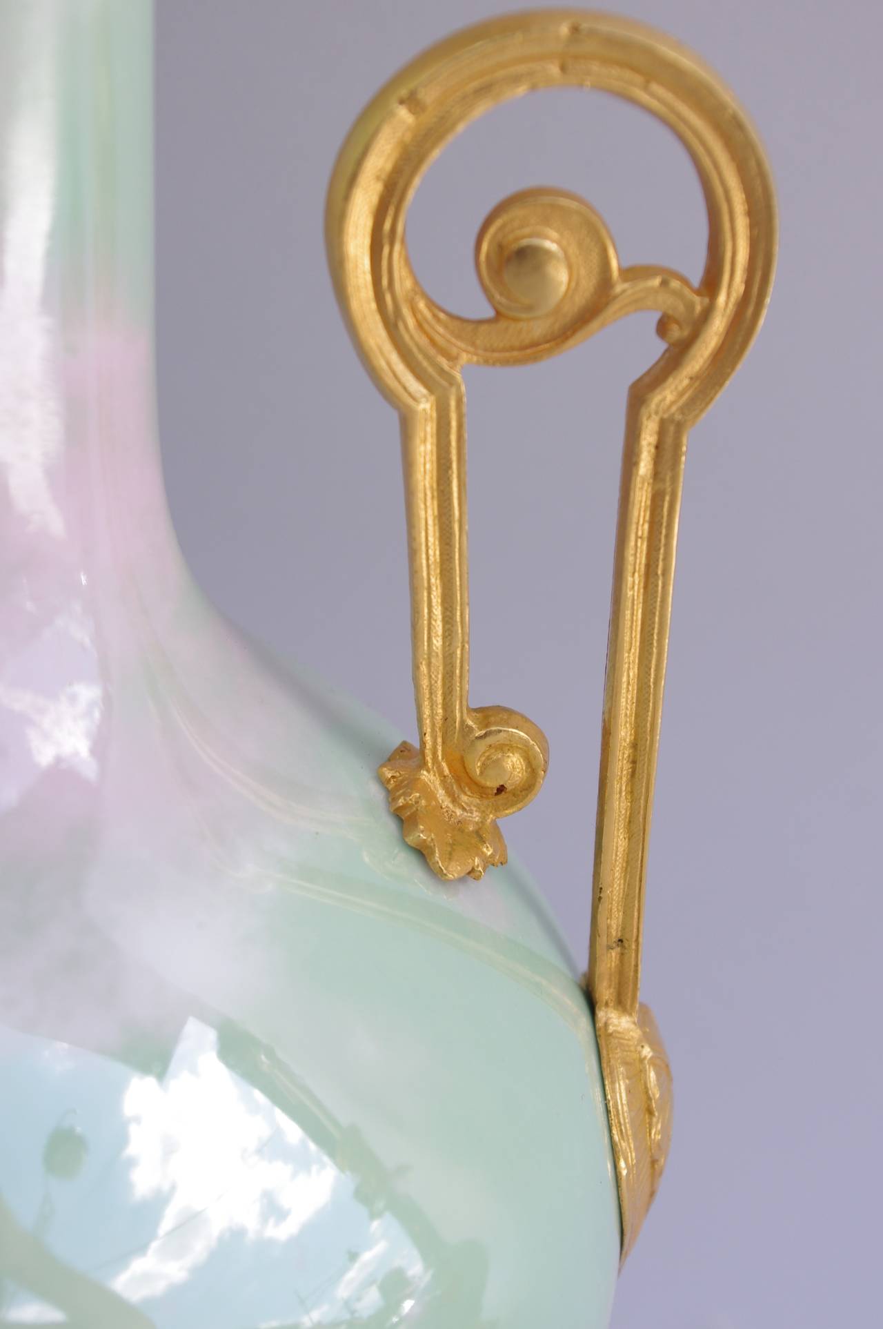 Coppia di lampade a bottiglia in porcellana celadon iridescente. Montatura in bronzo cesellato e dorato su una base circolare traforata decorata con cartigli e volute, due maniglie traforate e foglie d'acanto vicino al becco.
Impianto elettrico