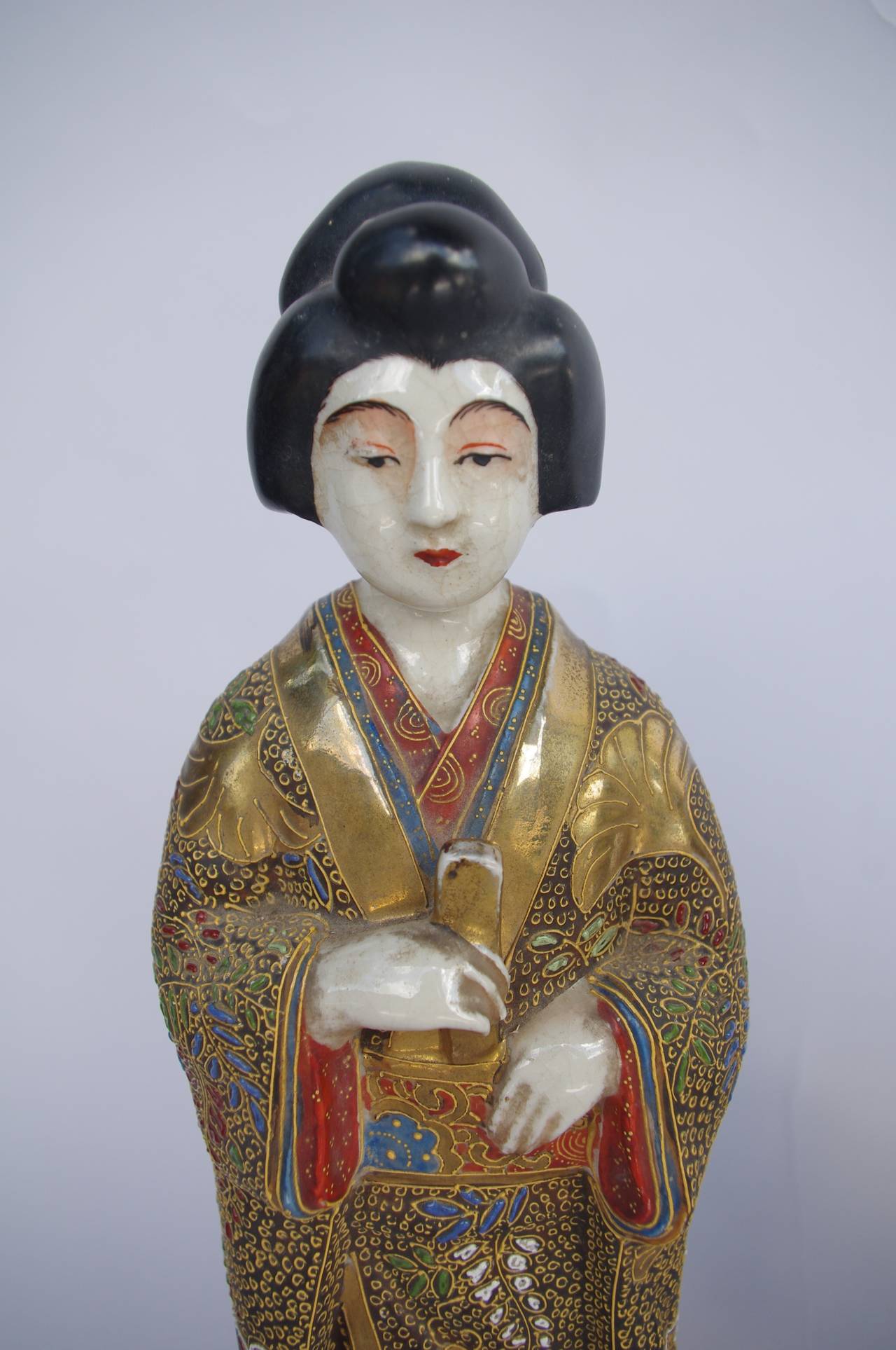 Pair of sculptures representing geishas dressed in gold and red and blue kimonos. One is hair dressed with a bun, naked hairs and the second one has a veil covering her hairs. 
Sculptures made in sandstone with polychromatic enamels on glaze and