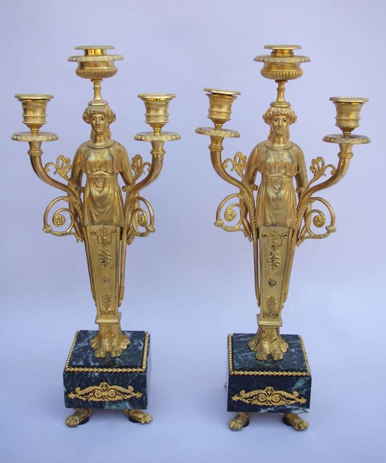 Pair of three fires chiseled and gilt bronze Louis XVI style candelabras. Four lion paws support a squared green marble base, on which are standing the feet of the central structure, a caryatid dressed in chiton with her legs sheath shaped. Her arms