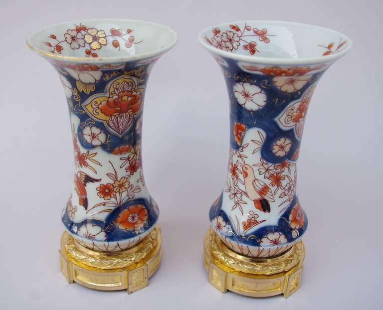 Pair of small Imari porcelain cone-shaped vases, standing on a circular gilt bronze base with a laurel torus. The vase is decorated with the traditional red and blue on a with background color, enhanced with gold, and shows some flowers like