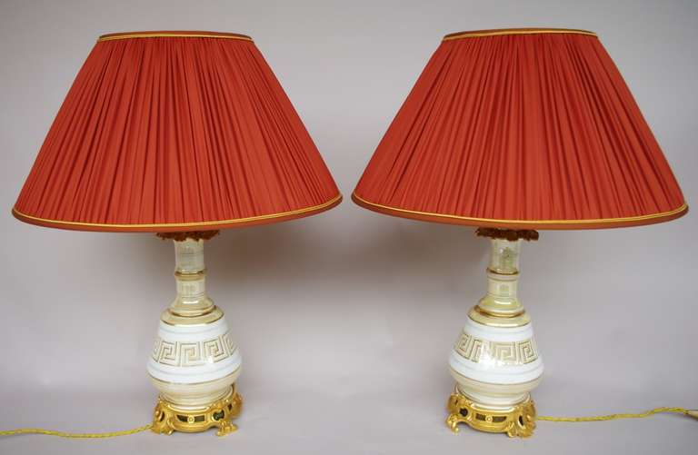 Pair of iridescent cream porcelain lamps decorated with a central frieze of cream and gold meander on a off-white banner. Chiseled and gilt bronze mount standing on an openwork Louis XV style circular base supported by four volutes legs. On the