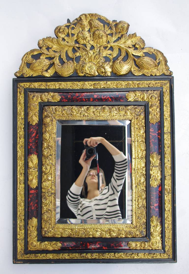 Napoleon III style beveled mirror with a triple frame in embossed and gilt brass. Different parts of the frame are adorned with blackened wood baguettes. The central frame is enhanced with red dyed tortoise shell.
The whole mirror is adorned with