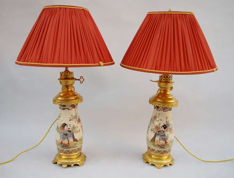 Pair of slightly bulged Satsuma earthenware lamps with a gilt bronze mount. Beige background decoration with geishas surrounded with dahlias in outside scenes and flanked by a palm leaves frieze beneath and alveoli frieze above. Chiseled and gilt