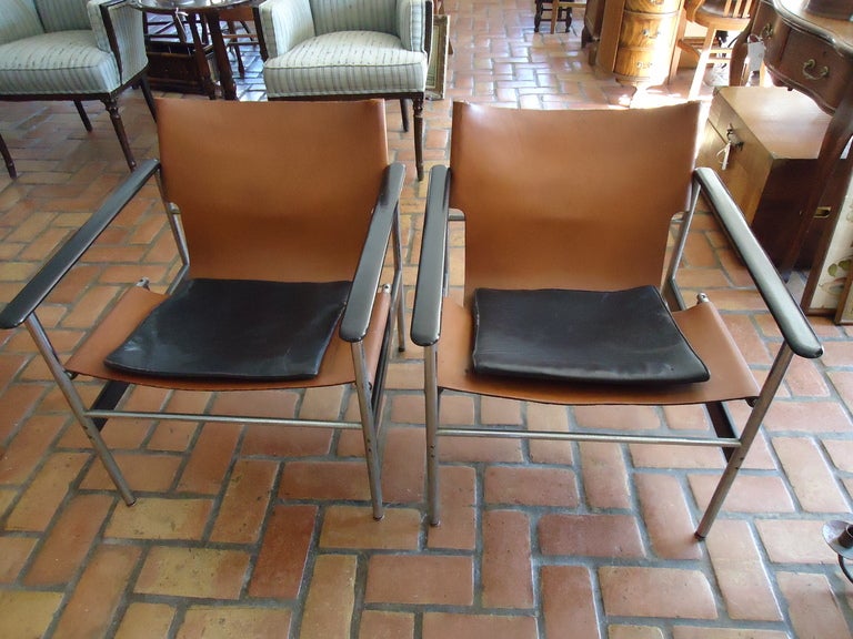 This pair of 657 sling lounge chairs have original tan leather sling seats with attached black leather seat cushion in a tubular frame with black resin coated aluminum armrests. Each with the oroginal Knoll paper label to the underside of the