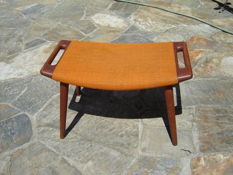 This Hans Wegner Papa Bear Ottoman comes in the original upholstery and is in excellent condition. The color is a weaved pumpkin colored wool upholstery. The wood is a solid Teak. Signed underneath. Use as a stool or ottoman.
