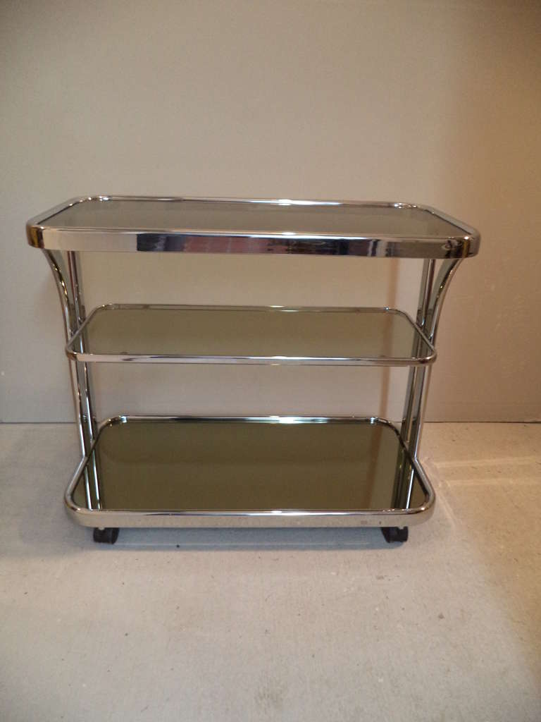 Milo Baughman mirrored chrome bar cart. Lower shelf is mirrored and the top two shelves are smoked glass. This exceptional piece will highlight any room decor and can be wheeled into any room.