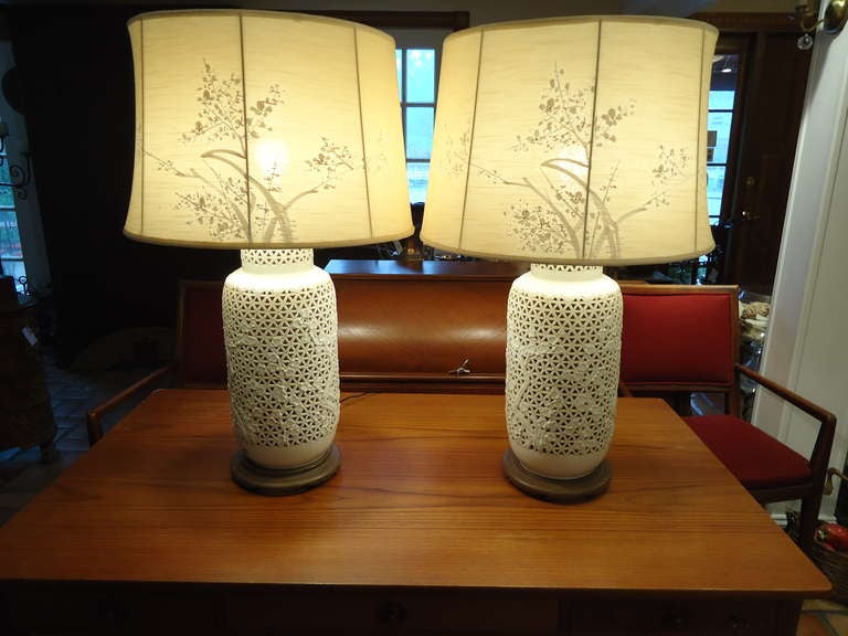 An outstanding pair of pierced porcelain Blanc De Chine lamps. These vintage ginger jar shaped lamps are reticulated with cherry blossom tree patterns and mounted on their original wooden carved bases. Both lamps have original metallic paper
