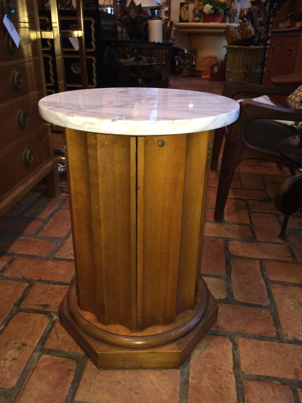 Round fluted wooden drum table or cabinet with marble top. With sculpted sides this cylinder table has two doors that open to a cabinet. There is a missing shelf inside that we can have made. The wood is light in tone. May be a fruitwood or Pecan.