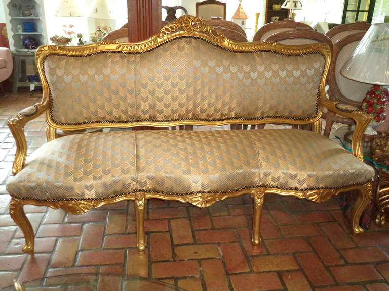 French gilt sofa in the style of Louis XVI with open scroll arms. Accentuated by a carved floral spray back and serpentine seat. Elegant and classic silk upholstery cover this canape.