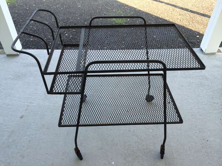 Fabulous Black wrought Iron Mid-Century Bar cart or Tea cart. Rolling wheels and sleek lines make up this Madmen cart. Double tier for serving both food and pouring drinks. Saddled in space near handle to hold all your bottles and keep them safe