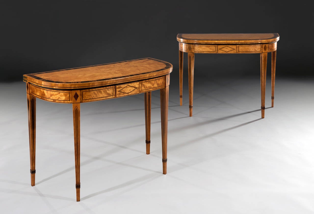 The D-shaped satinwood tops are cross banded with wide coromandel bands, cross banded with satinwood, boxwood and ebony stringing.  The tables have been recently re-baized in a deep burgundy colour with blind tooling. The shallow frieze is decorated