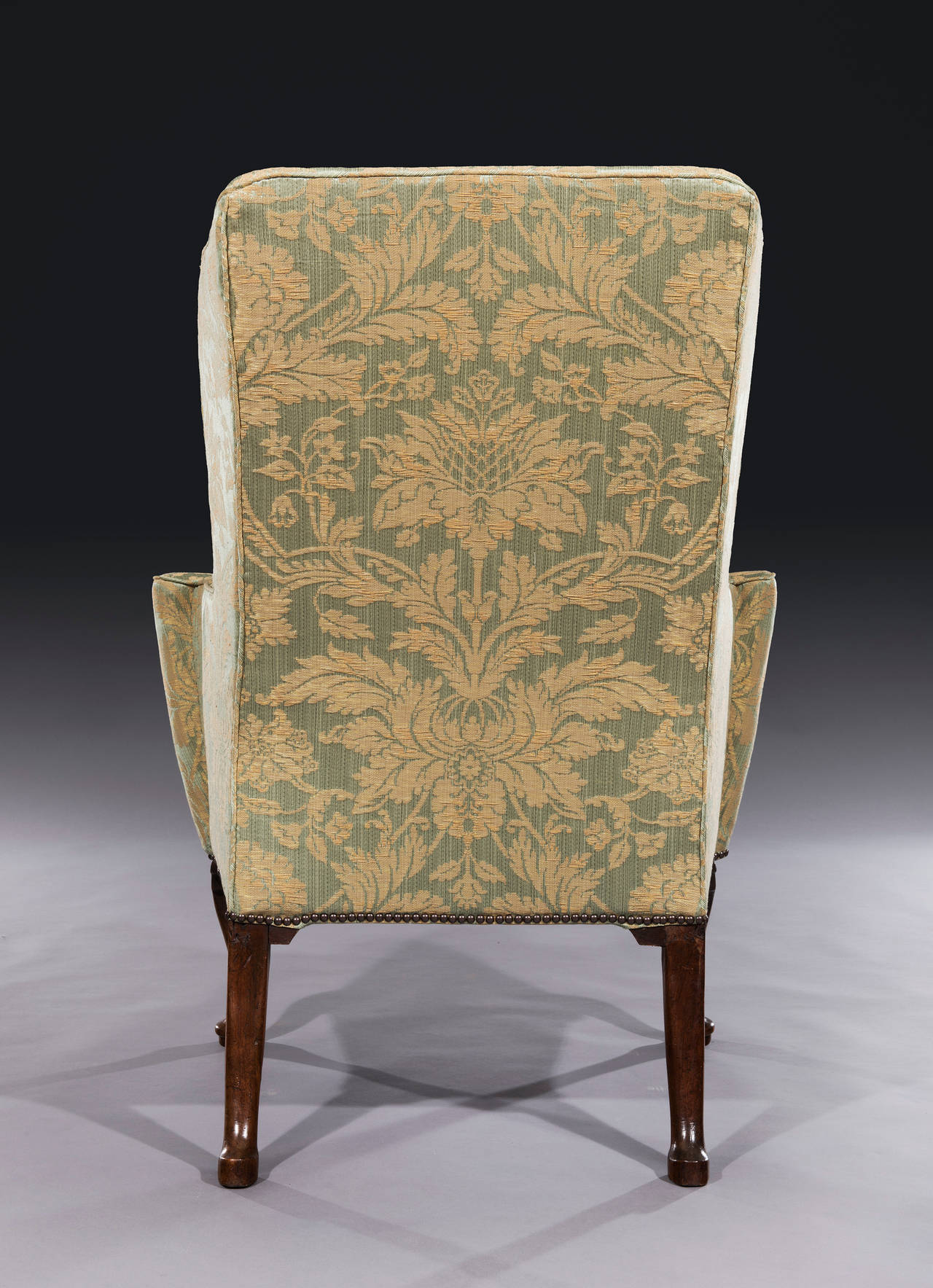 The winged back armchair has a tall backrest and shaped sides scrolling down seamlessly to out-scrolled arms on a bow-fronted seat and stands on original cabriole front legs and outswept back legs.