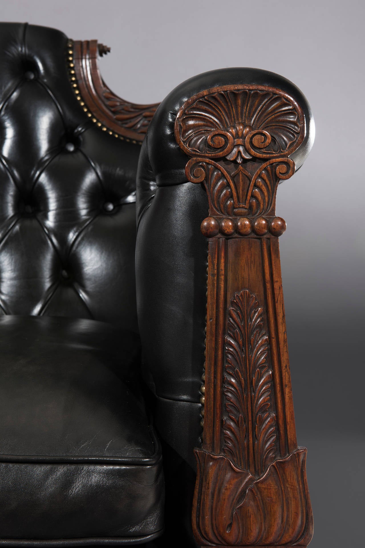 This stunning Regency period double-ended settee with a deep buttoned black leather finish and three removable cushions has crisply carved leaf decoration and turned scrolled ears to the back. The front arm supports are carved with acanthus and
