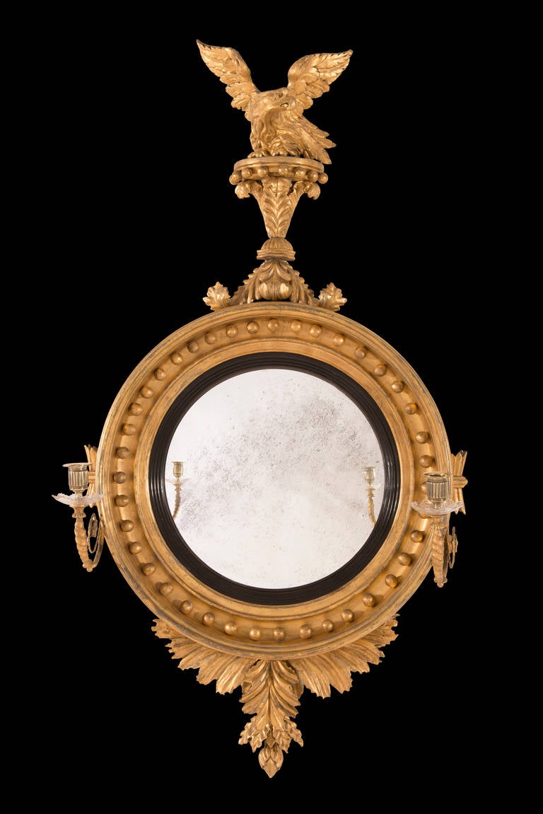 The giltwood and gesso convex mirror has a reeded ebonized slip and eagle surmount. It has single scroll branches with the original glass drip pans and gilt brass candleholders. The plate is original to the frame. 

Thomas Fentham (d.1808) was a