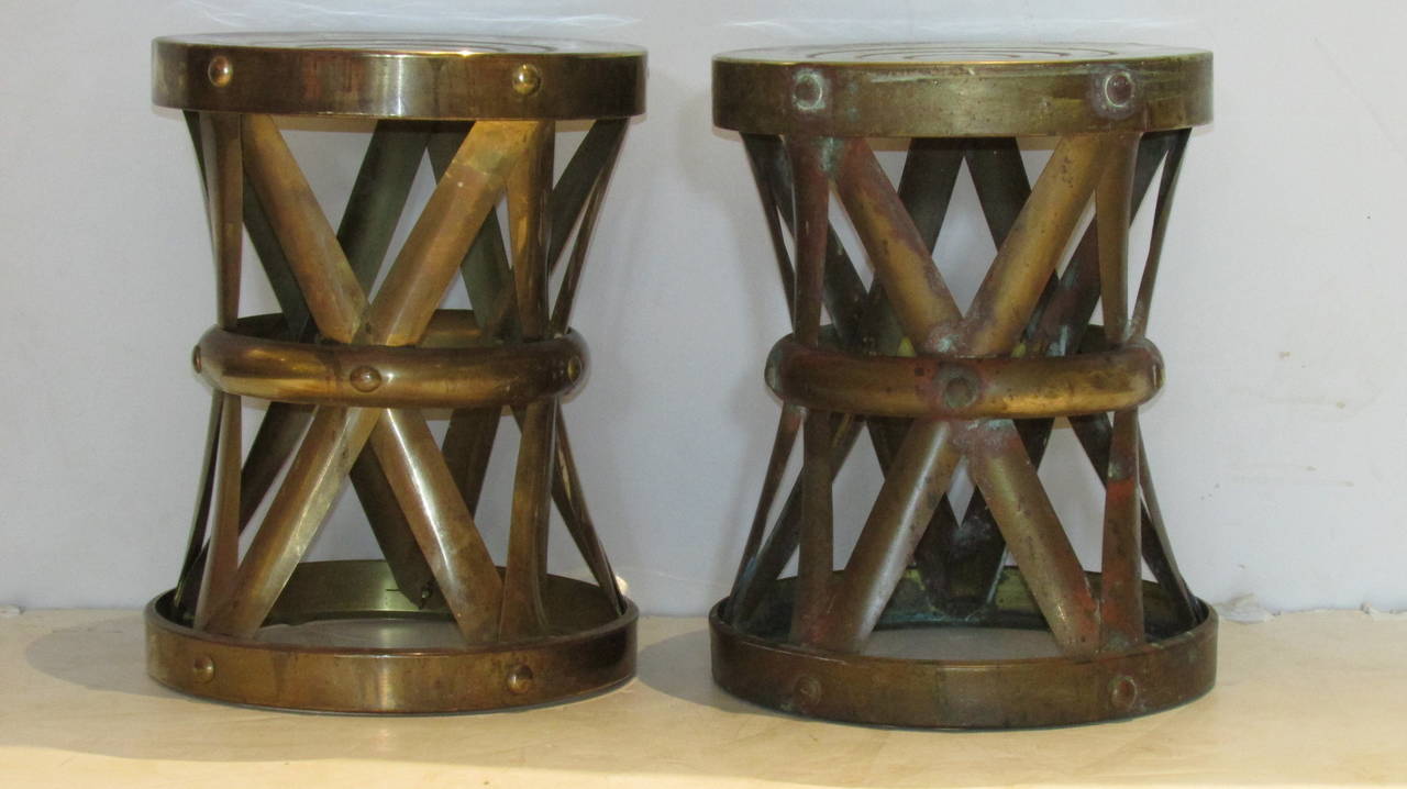 A pair of 1970's brass X form riveted drum stools or side tables - the tops with a concentric circle design. Both are in nicely aged oxidized patina with areas of verdigris. In the style of Sarreid Ltd. Spain