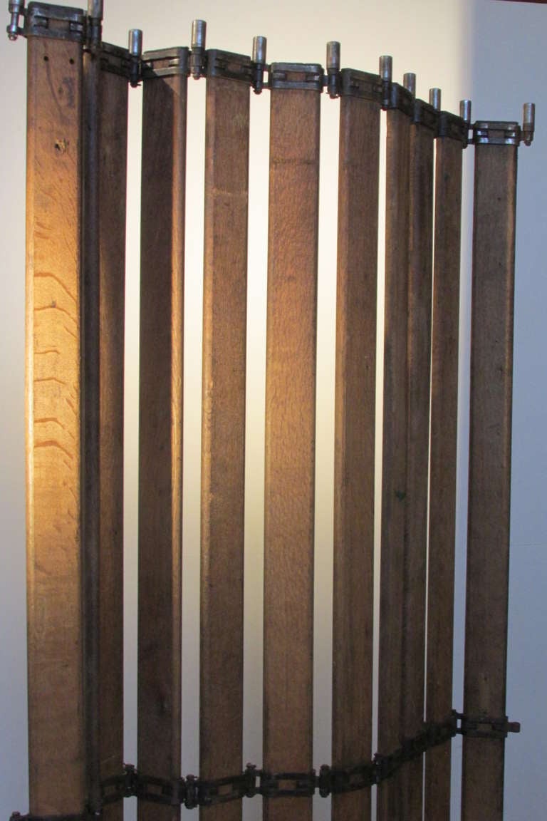A folding wood slat and nickle finished steel mounted industrial freight elevator door -  staged with flat circular iron discs at bottom that allow for use as a free standing screen. This can be maneuvered into many contoured positions. The slatted
